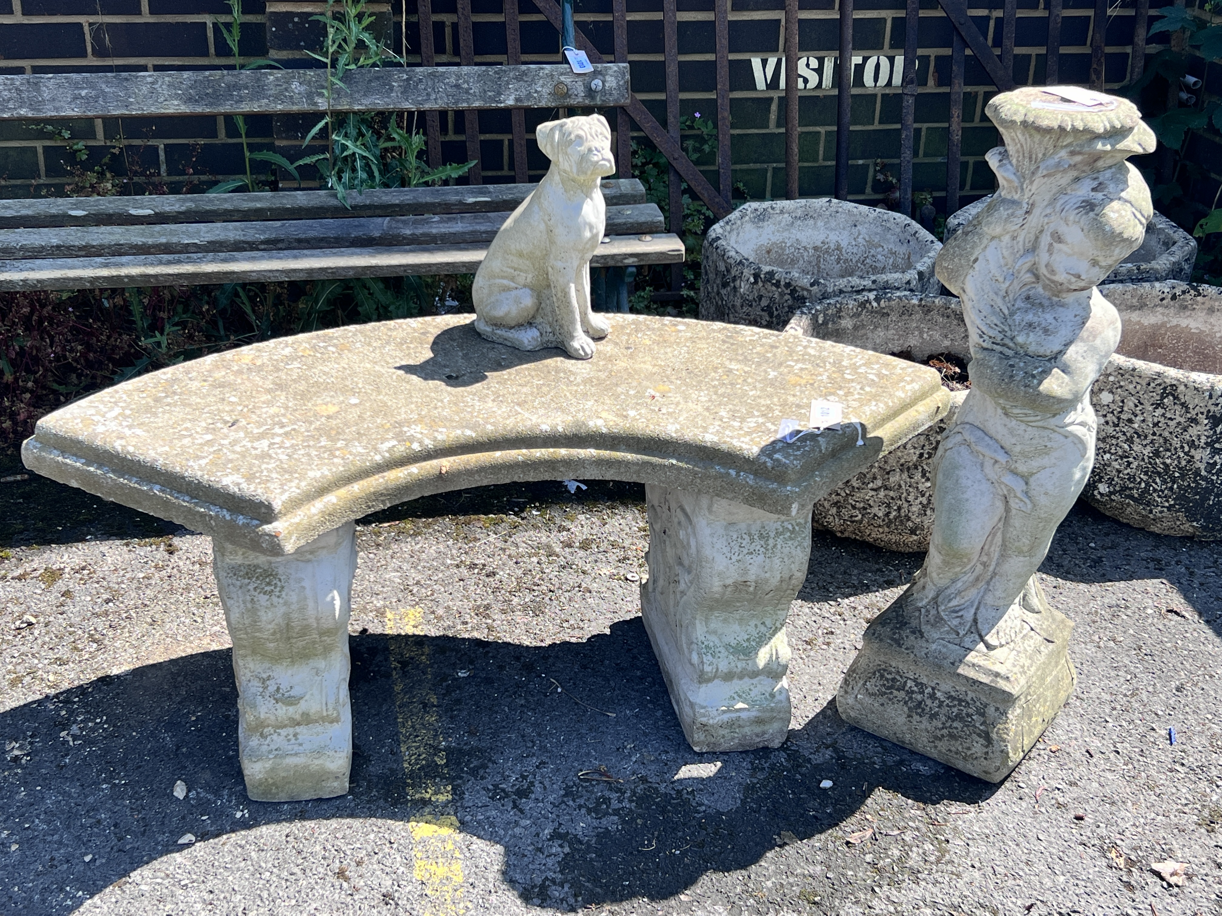 A small reconstituted stone curved garden bench, width 110cm, height 44cm, together with a stone pedestal and a small dog ornament